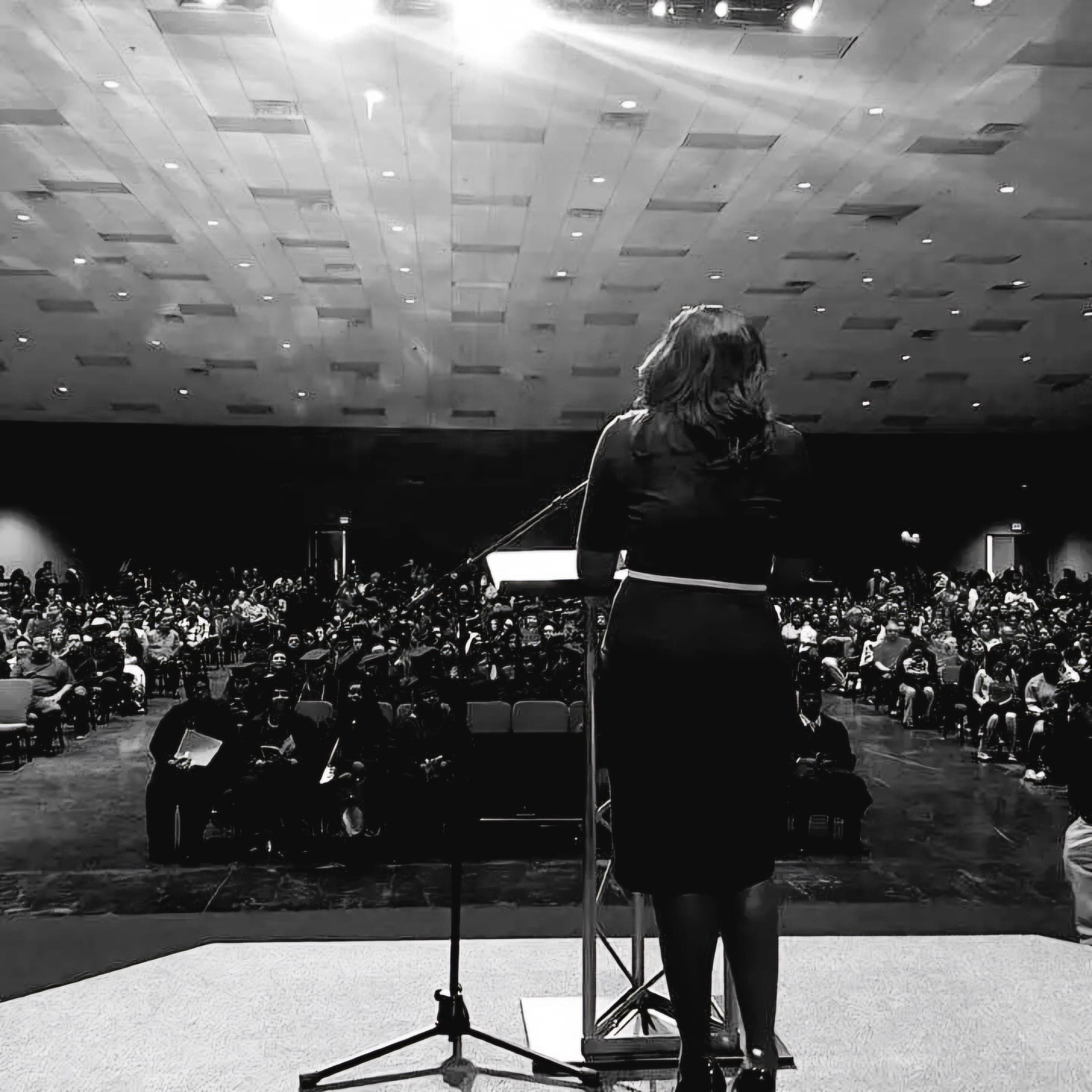 Dr. Laide R. Alexander on stage at the lectern, facing a full auditorium